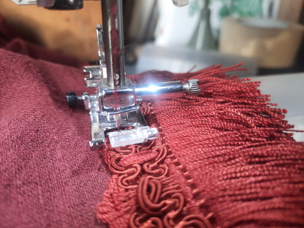 pied presseur d'une machine a coudre sur un tissus rouge entrain de coudre un galon